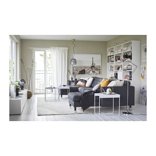 Sala de estar moderna con sofá LANDSKRONA gris, estantería blanca, mesa de centro de vidrio y cortinas verdes. Gran foto de parís en la pared.