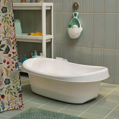 Bañera para bebés con bordes suaves, base antideslizante, gancho para colgar, color blanco, colocada sobre azulejos azules, junto a cortina de ducha floral.