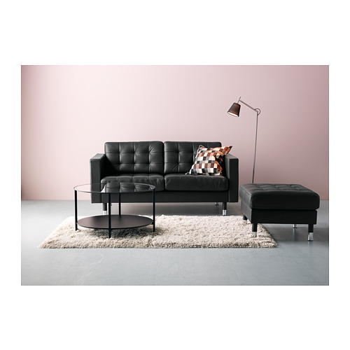 Sala de estar moderna con sofá de cuero negro, mesa de centro de vidrio, lámpara de pie y alfombra peluda en pared rosa.