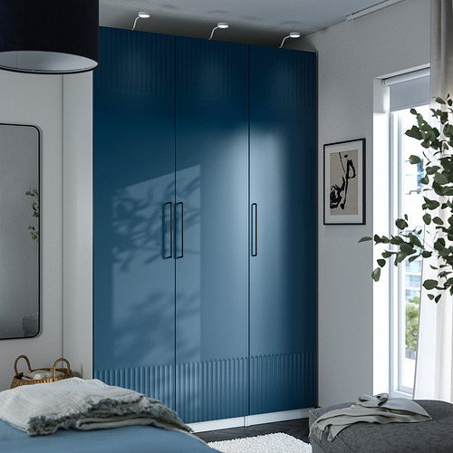 Armario PAX azul junto a ventana con lámpara. Cama, espejo, planta en habitación minimalista.