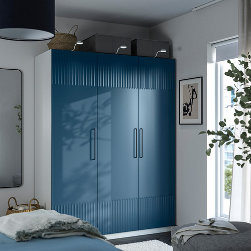 Dormitorio moderno con armario alto PAX azul, tiradores plateados, luz natural, planta, ropa de cama ligera