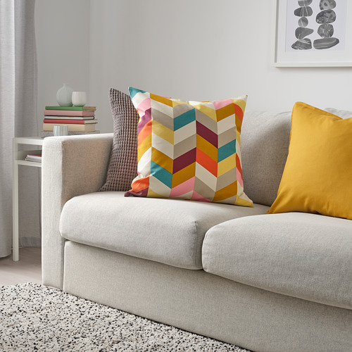 Cojín de chevron y almohada amarilla en sofá gris, libros y jarrón sobre mesa blanca.