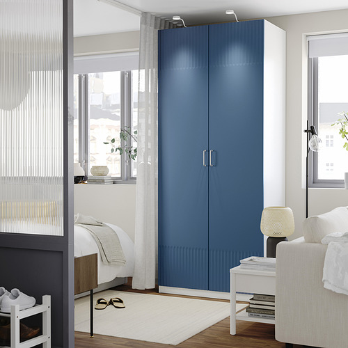 Dormitorio moderno con armario PAX azul, gran ventanal, alfombra blanca y decoración minimalista.