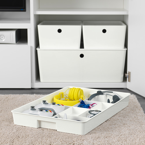 Bandeja organizadora blanca con mandos de juego y accesorios, guardados en compartimentos. Parte del sistema KUGGIS para organizar artículos más pequeños.