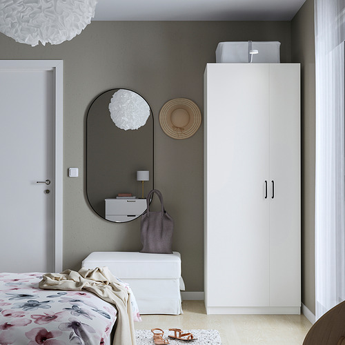 Dormitorio moderno con armario PAX blanco, espejo redondo y ropa de cama floral contra una pared oscura.
