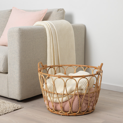 Cesta de mimbre cerca de un sofá con mantas beige y rosas, que muestra el almacenamiento y el uso decorativo en un espacio habitable.