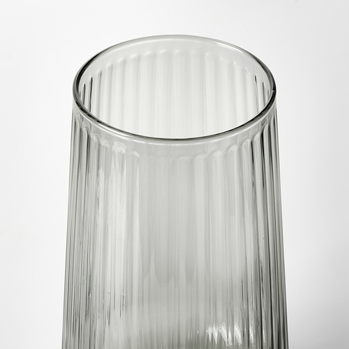 Jarrón de vidrio transparente con textura acanalada, de pie sobre fondo blanco.