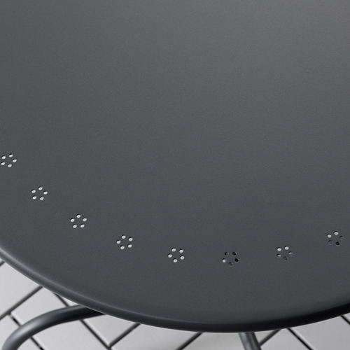 Primer plano de una mesa redonda de metal negro con orificios de drenaje espaciados uniformemente, diseñada para uso en exteriores.