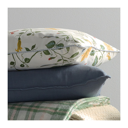 Vista frontal de dos almohadas apiladas: parte superior blanca con estampado floral verde, parte inferior azul, sobre manta texturizada.