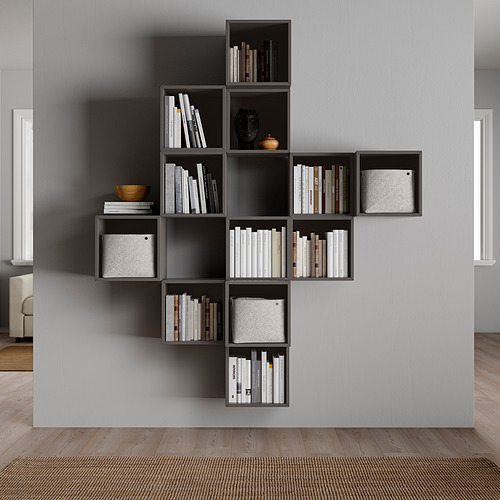Moderna estantería gris montada en la pared, llena de libros y artículos decorativos. Diseño asimétrico con múltiples compartimentos.
