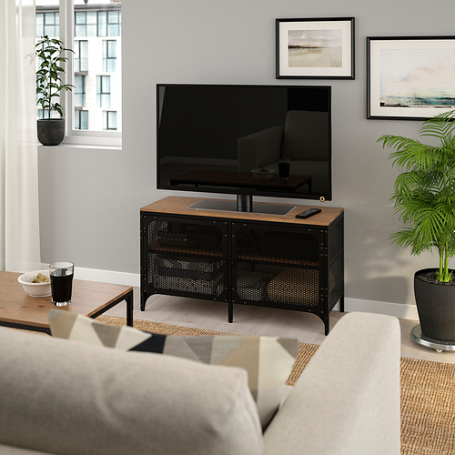 Mueble de tv FJÄLLBO con puertas de malla bajo pantalla plana, en salón rústico con sofá y plantas.
