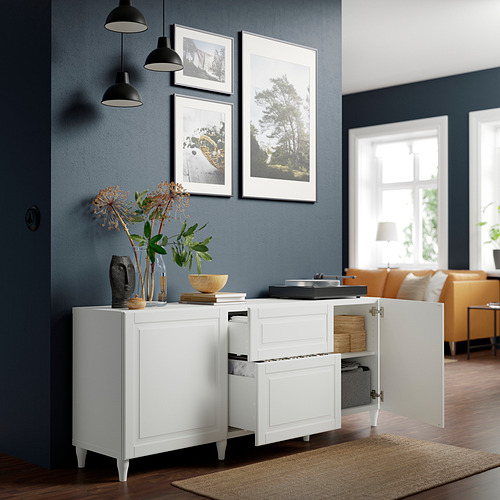 Mueble de almacenaje blanco BESTÅ con estantes, cajones y cierre suave. Fijado a la pared azul oscuro, sosteniendo decoración y cajas.