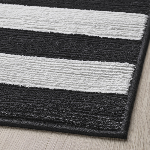 Alfombra de rayas blancas y negras con superficie texturizada, colocada sobre suelo de madera; Parece suave y de alta calidad.