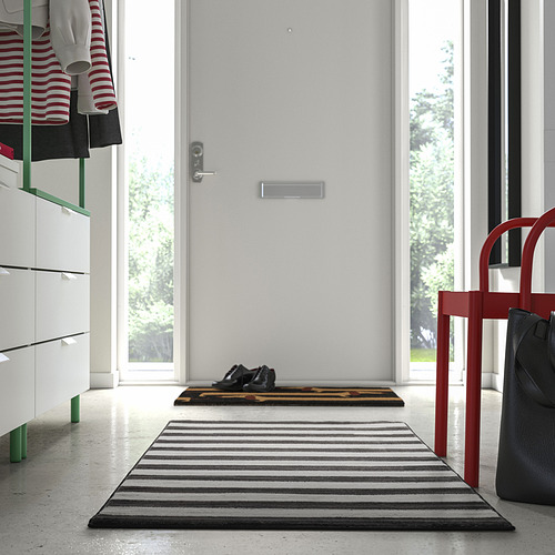 Entrada moderna con pequeña alfombra blanca y negra, silla roja, bolso negro.