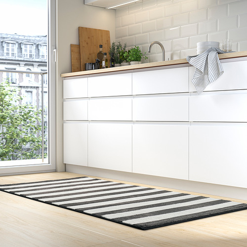 Cocina moderna con armarios blancos, gran ventanal, alfombra gris a rayas, rayas blancas y negras, poliéster reciclado suave.