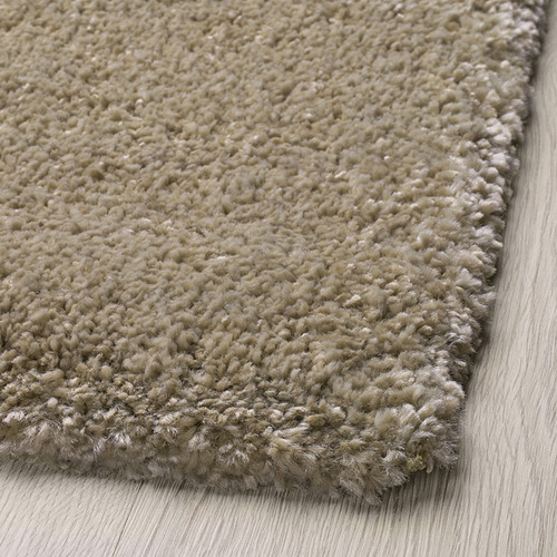 Alfombra suave y peluda de color claro colocada sobre suelo de madera, que muestra su textura gruesa y acogedora.
