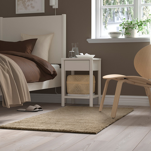 Un acogedor dormitorio con una alfombra blanca, una cama marrón, una mesa blanca y una silla de madera.