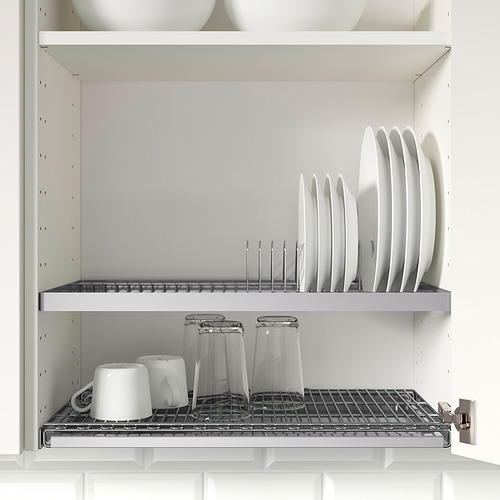 Armario de pared abierto con platos almacenados en una rejilla de drenaje, debajo hay vasos y tazas en una rejilla de alambre, colocada en una cocina limpia y blanca.