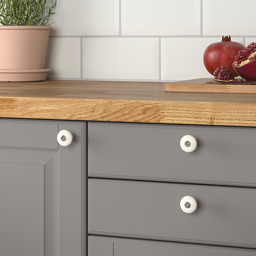 Encimera de cocina con cajones grises, encimera de madera, pomos blancos, granadas y planta.