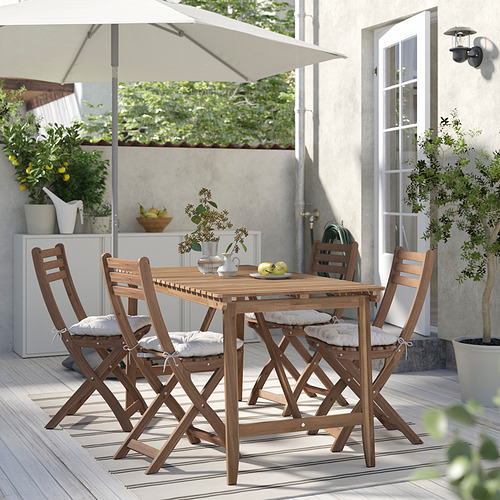 Patio con mesa de acacia, sillas plegables, alfombra a rayas y plantas en cubierta de madera.