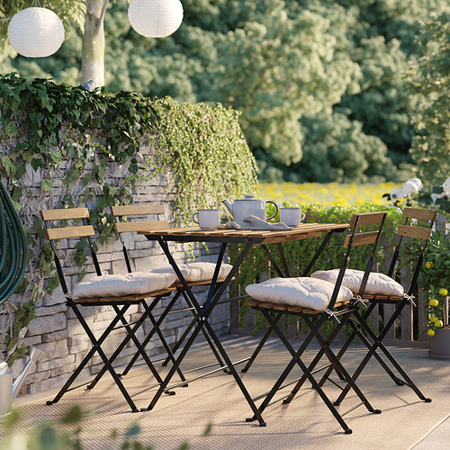 Pequeño patio con mesa de madera, 4 sillas, cojines. Rodeado de vegetación, acogedores asientos al aire libre.
