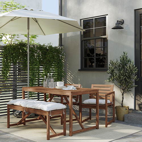 Imagen NÄMMARÖ juego de mesa y sillas de exterior, madera de acacia, cojines crema, en un patio.