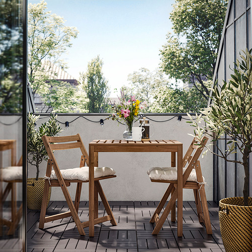Patio con mesa NÄMMARÖ, sillas acolchadas blancas, plantas y luces.