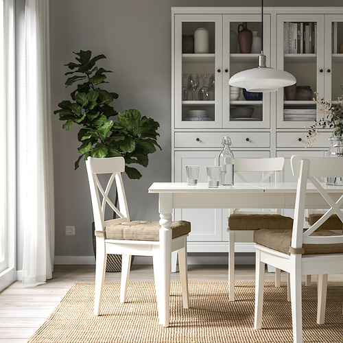 Acogedor comedor con muebles blancos y gran silla almohadilla beige. Mueble de vegetación y porcelana con platos y jarrones.