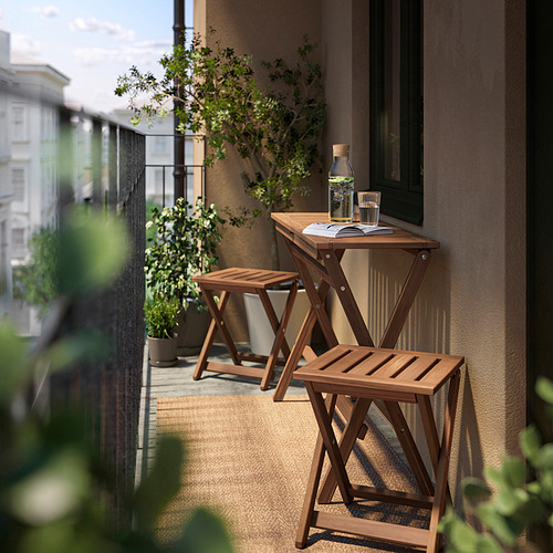 Pequeño balcón con mesa y taburetes de madera marrón NÄMMARÖ, jarra de cristal y plantas.