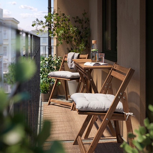 Pequeño balcón con mesa y sillas de madera NÄMMARÖ, asientos acolchados, ambiente al aire libre.