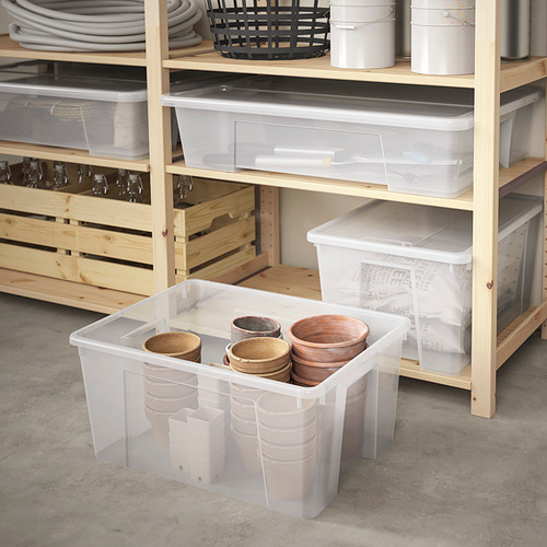 Gran caja de almacenamiento SAMLA transparente en estante con tazas de madera, rodeada de cajas similares y artículos en estantes.