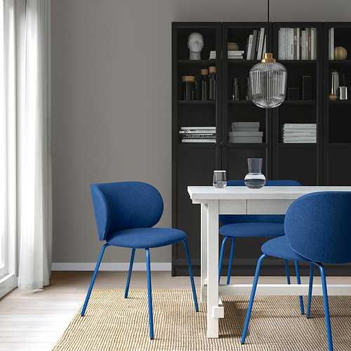 Moderno juego de comedor con sillas azules, patas metálicas, estantería, cortina, lámpara colgante.