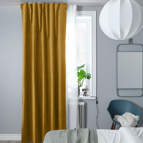 Cortinas mostaza en riel, ventana luminosa, paredes azules, radiador blanco, planta verde, silla azul con manta blanca.