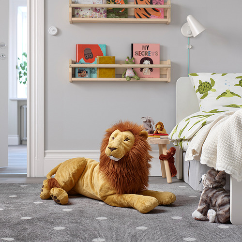 Un gran juguete de peluche de león amarillo yace en el suelo de la habitación del niño, rodeado de libros, juguetes pequeños y cama.