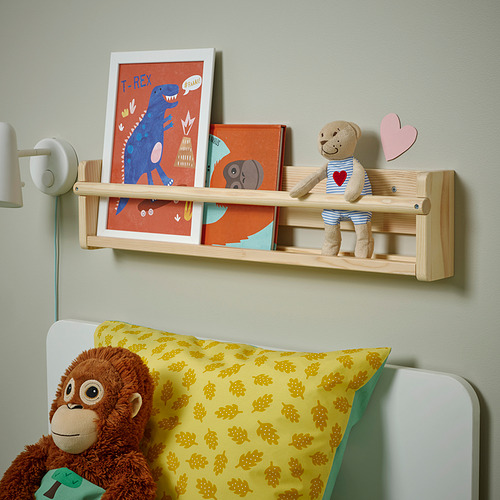 Un estante de madera con libros ilustrados y un osito de peluche de peluche, con un gran mono de peluche sobre una cama con una almohada amarilla estampada.