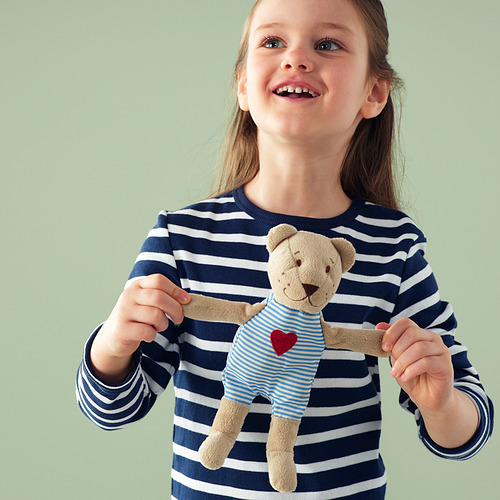 Una niña que sostiene un osito de peluche con una camisa de rayas azules y blancas con un corazón rojo.