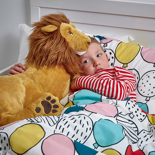 Niño abrazando un gran juguete de león de peluche en la cama con un patrón colorido.