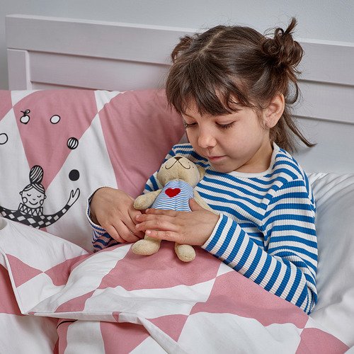 Una niña en pijama a rayas se sienta en una cama rosa y blanca, sosteniendo un oso de peluche, mostrando su naturaleza reconfortante.