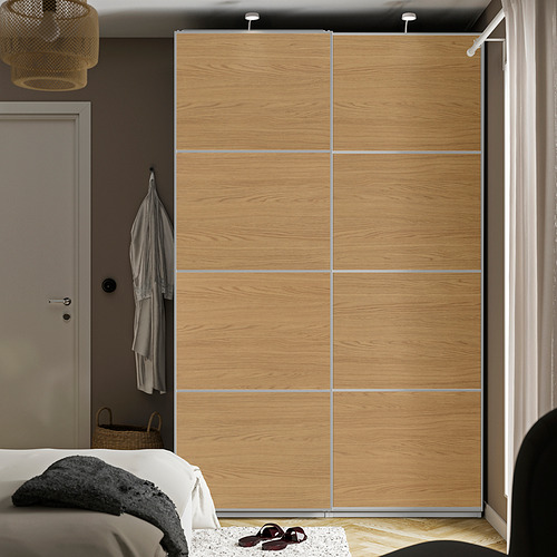 Dormitorio moderno con armario alto PAX , puertas correderas y cama de manta mixta. Almacenamiento colgante, estantes visibles, cesta de mimbre debajo.