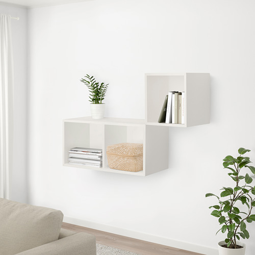 Sala de estar moderna con paredes blancas, sofá beige, estanterías con libros, plantas y caja de bambú. Planta de suelo cerca del sofá.