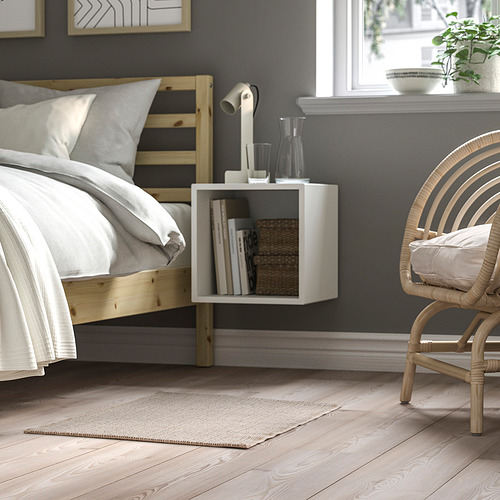 Acogedor dormitorio con cama de madera, ropa de cama blanca, estantería flotante, silla de mimbre, alfombra beige.