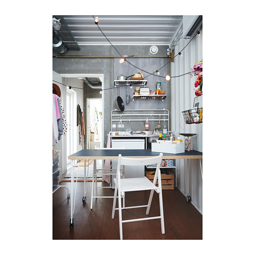Cocina pequeña y elegante con paredes grises, una silla blanca, una mesa de metal y estantes organizados con luces colgantes.