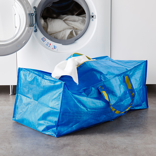 Bolsa grande FRAKTA azul con asas amarillas contiene toallas blancas cerca de la lavadora abierta.