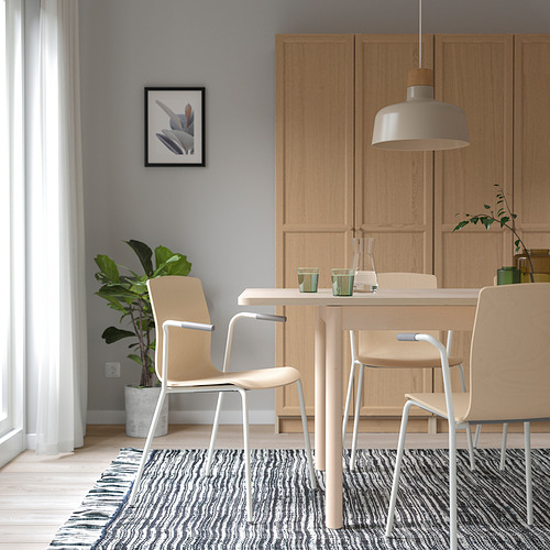 Comedor moderno con mesa, sillas y armarios de madera. Lámpara colgante, cuadro enmarcado, planta y alfombra texturizada.