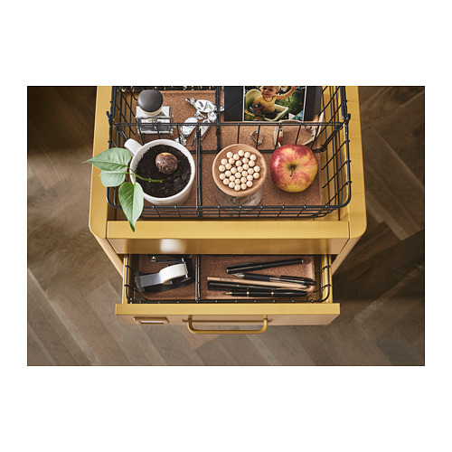 Carro de almacenamiento amarillo IDÅSEN con cesta de alambre, planta en maceta, taza, manzana, cuenco y bolígrafos en el cajón.