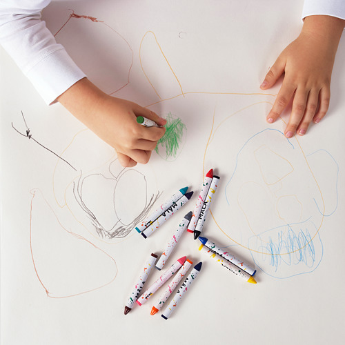 Un niño dibuja con crayones de colores en papel; seis lápices de colores MÅLA yacen cerca.
