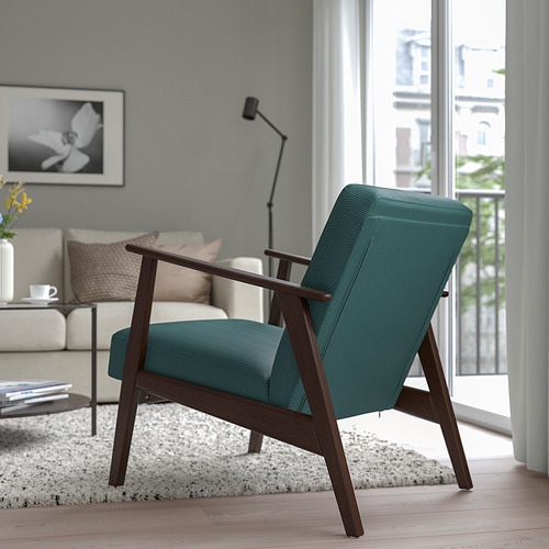 Sillón tapizado de estilo retro verde azulado con patas de madera se encuentra junto a una ventana en una acogedora sala de estar.