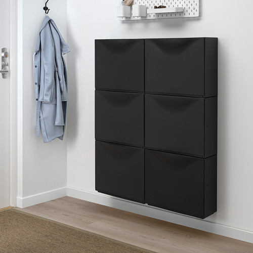 El armario TRONES negro ofrece un almacenamiento poco profundo, ideal para espacios pequeños. Sujeta el gancho de pared con chaqueta azul.