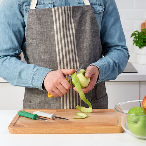 Persona pelando manzana verde con un pequeño cuchillo de cocina de UPPFYLLD colocado en una tabla de cortar de madera. Tazón de manzanas peladas cerca.