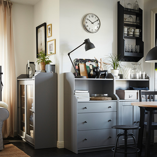 Sala de estar moderna con gabinetes grises, un reloj de pared redondo, lámpara negra y elementos decorativos, con una mesa de comedor y sillas al fondo.